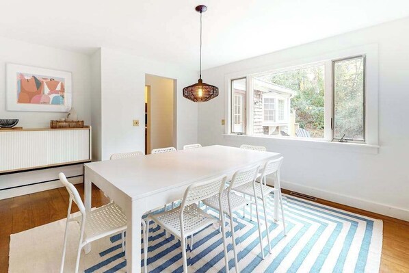 Zona pranzo con tavolo bianco, sedie bianche, tappeto a righe blu e bianco e lampadario.