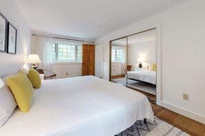 A bedroom with a large bed, a wooden door, a mirror, and a window. - Peaceful half-acre home near ocean, dining & shops and a fire pit (Wellfleet)