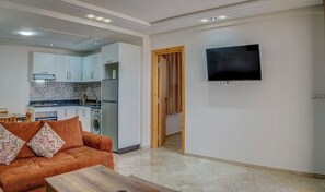 A living room with a sofa, a coffee table, a TV mounted on the wall, and a kitchen area with cabinets and appliances. - Studio with Terrace Overlooking the Beach (Tamraght)