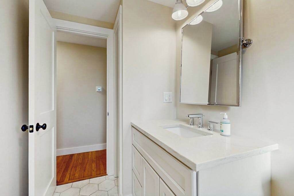 Un baño con tocador blanco, espejo y puerta de ducha.