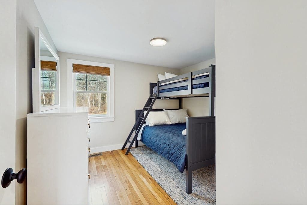 Un dormitorio con una cama litera, una ventana con persianas, una puerta y una lámpara.