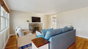 A living room with a sofa, a television, a fireplace, and a window. - Peaceful Maravista escape with AC, W/D, yard, walk to Great Pond, & breezy charm (Falmouth)