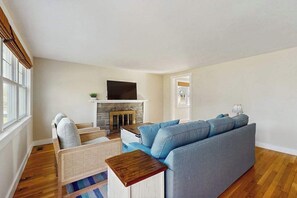 Ein Wohnzimmer mit einer Couch, einem Fernseher, einem Kamin und einem Fenster.