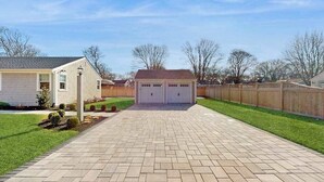 A residential driveway leading to a garage with a wooden fence and a house on the left. - Peaceful Maravista escape with AC, W/D, yard, walk to Great Pond, & breezy charm (Falmouth)