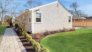 A single-story house with a sloped roof, a front porch, and a well-maintained lawn. - Peaceful Maravista escape with AC, W/D, yard, walk to Great Pond, & breezy charm (Falmouth)