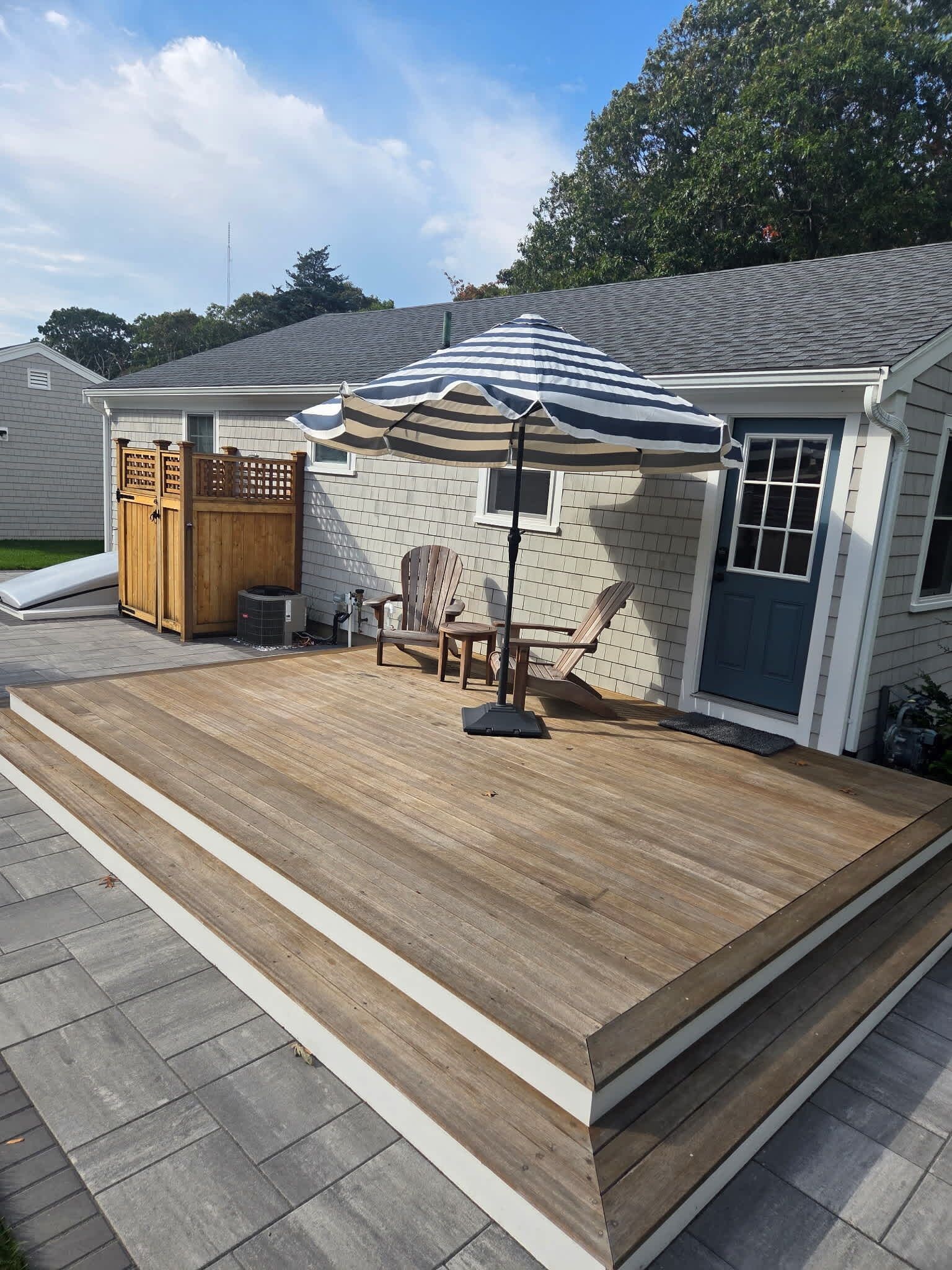 A deck with a wooden floor, a striped umbrella, and two Adirondack chairs.