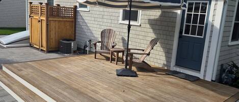 A deck with a wooden floor, a striped umbrella, and two Adirondack chairs.