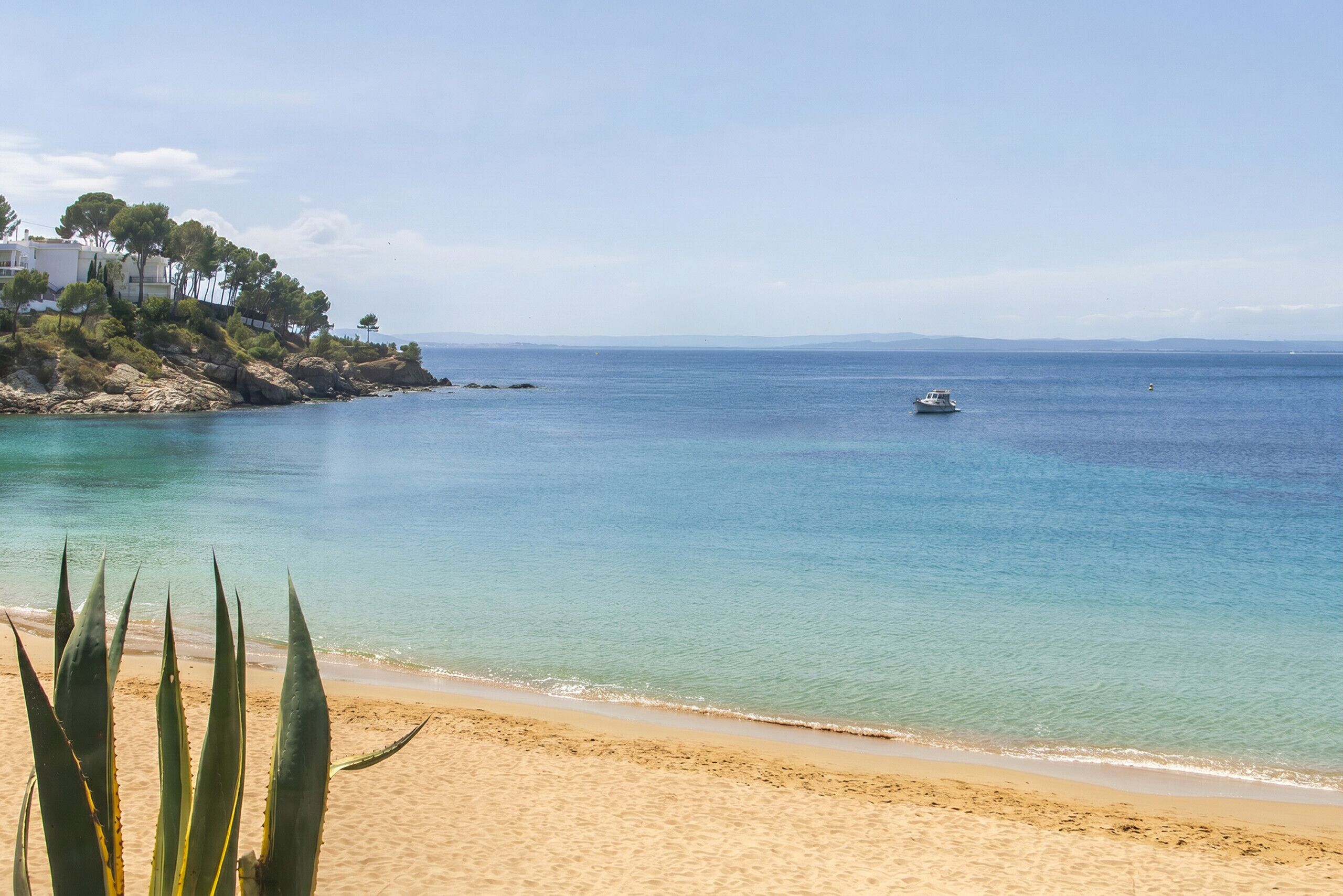 Una playa con agua cristalina, un barco y edificios en un acantilado rocoso.