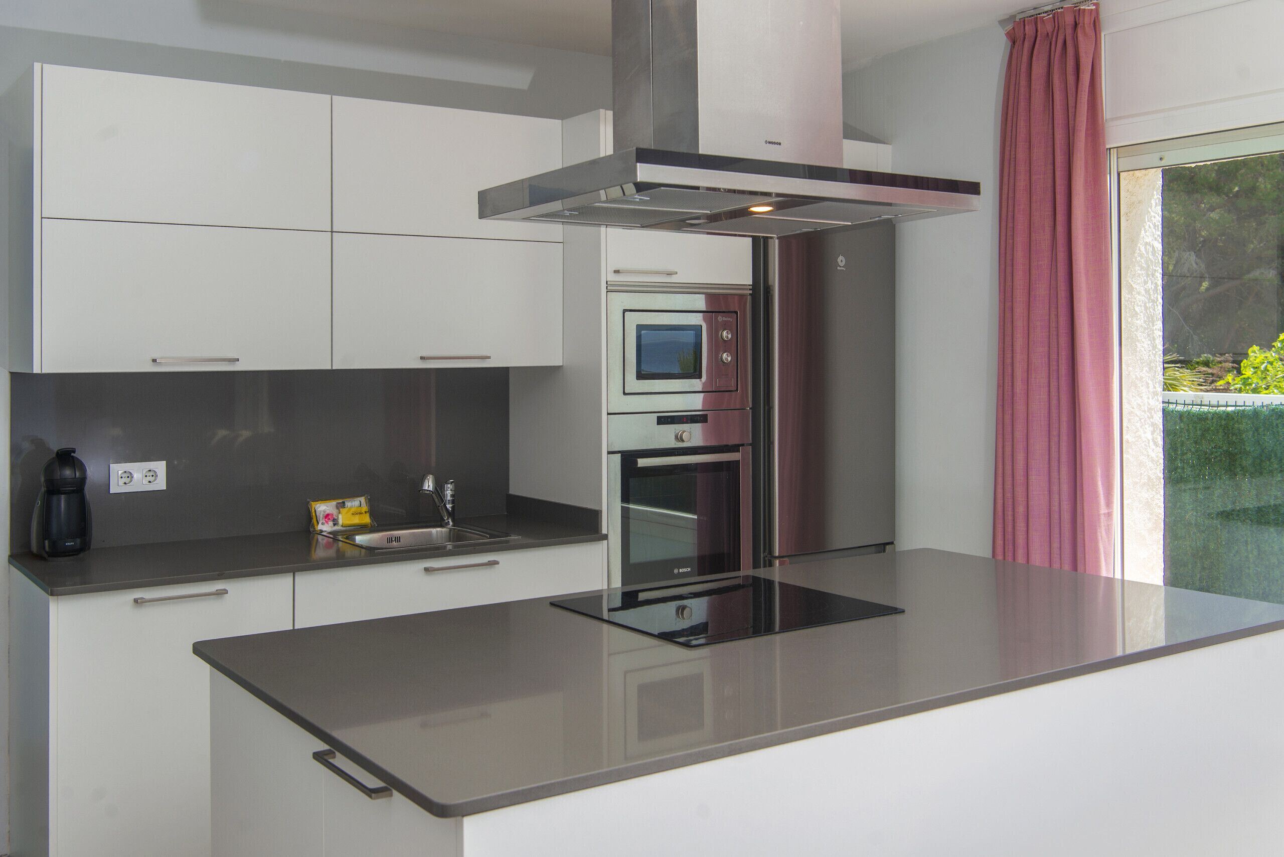 Una cocina moderna con horno empotrado, extractor de humos y una isla grande con encimera de vidrio.