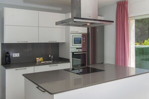 A modern kitchen with a built-in oven, a range hood, and a large island with a glass top. - WELCS VILLA 346 MADRAGUE first sea line (Rosas / Roses)
