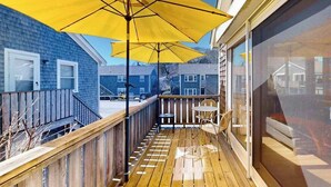 Una terraza de madera con un paraguas amarillo, una mesa y sillas.