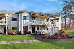 A multi-story building with a front porch, a staircase, and a small garden area. - Modern fairway condo with open layout, private patio, AC & washer/dryer (Brewster)