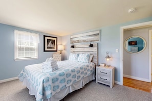 A bedroom with a bed, bedside tables, a nightstand, a lamp, a framed picture, a window with blinds, and a door with a mirror. - Inviting bungalow with fireplace, patio, firepit, full kitchen, & W/D (Yarmouth)