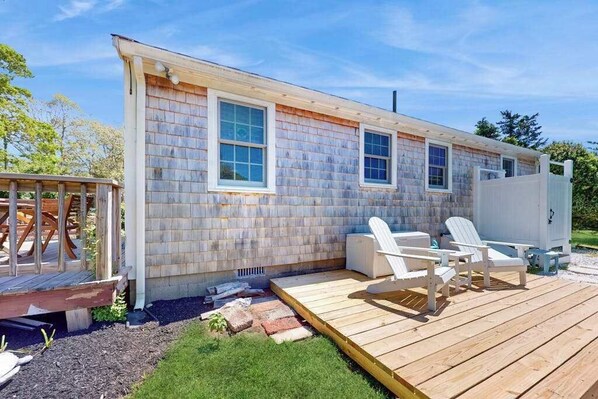 Una casa de un piso con una terraza, mobiliario exterior y un cobertizo pequeño.