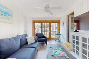 A room with a sofa, armchair, ceiling fan, and a view through a glass door.