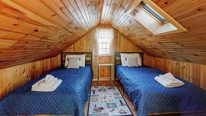 Une chambre mansardée chaleureuse, avec deux lits, une lucarne et une petite fenêtre.