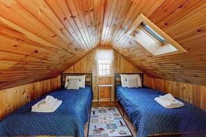 Ein gemütliches Schlafzimmer im Dachgeschoss mit zwei Betten, einem Oberlicht und einem kleinen Fenster.