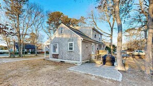 Une maison à deux étages avec un porche à l’avant, un garage et une cour avec des arbres.