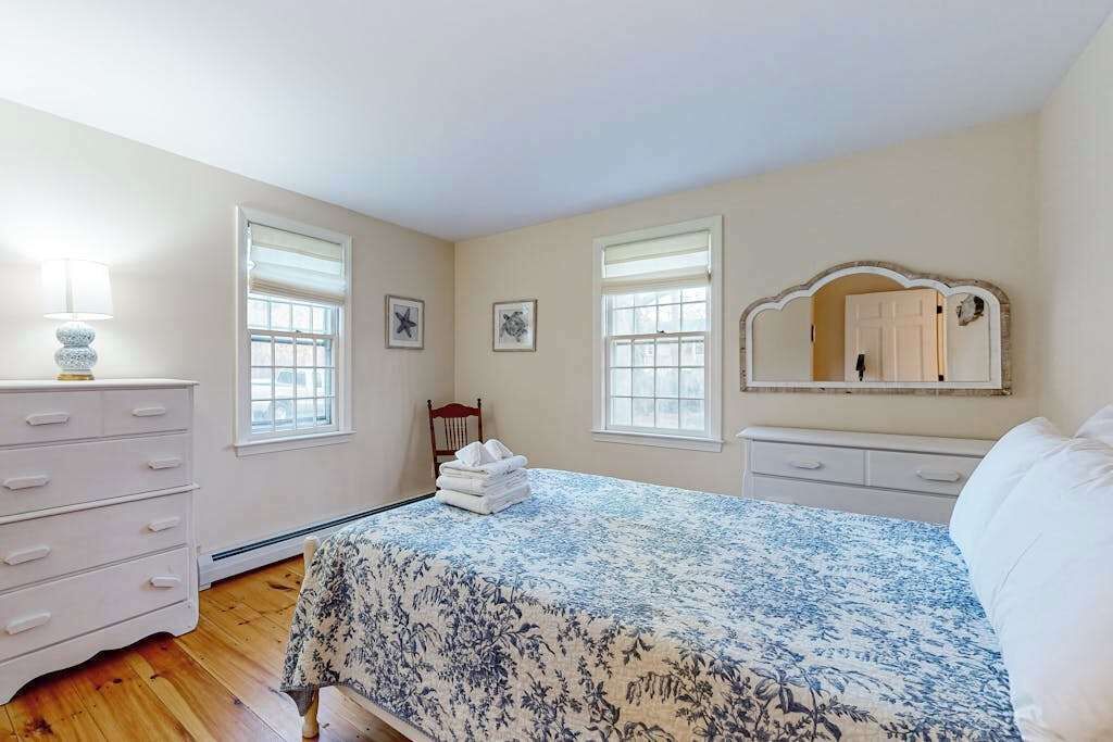 A bedroom with a bed, dresser, and two windows.