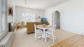A spacious living room with a round table and chairs, a sofa, a television, and a door leading to another room.