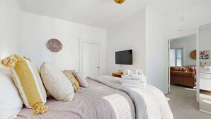 A bedroom with a bed, a TV, a door, and a hallway leading to another room.