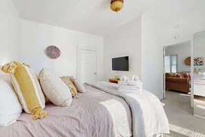 Une chambre à coucher avec un lit, une télévision, une porte et un couloir menant à une autre pièce.
