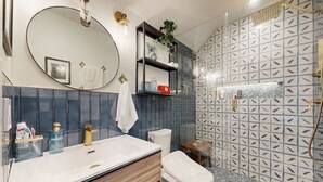 Een badkamer met een ronde spiegel, een witte wastafel, een toilet en een douche met een behangetje op de muur.