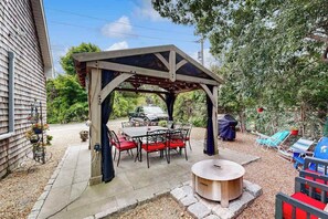A covered patio with a table and chairs, a fire pit, and outdoor seating.