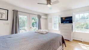 Une chambre à coucher avec un lit, un ventilateur de plafond, une télévision, une commode et une fenêtre.