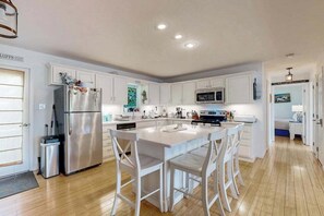 A modern kitchen with white cabinetry, a stainless steel refrigerator, a central island with bar stools, and a microwave above the stove.