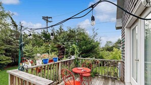 Une terrasse en bois avec une table et des chaises, entourée de verdure et d’une maison.