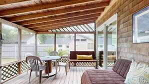 Une véranda couverte avec un plafond en bois, une table avec des chaises, un canapé et un banc.