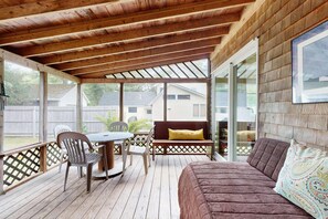 Eine überdachte Veranda mit Holzboden, einem Tisch mit Stühlen, einer Couch und einer Bank.
