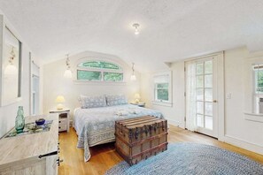 Ein Schlafzimmer mit Bett, Kommode, Fenster und Tür.