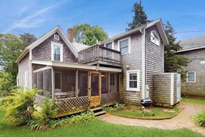 Ein zweigeschossiges Haus mit einer überdachten Veranda, einer kleinen Terrasse und einem Hinterhof mit Grill.
