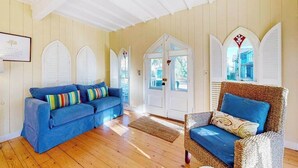 Ein Zimmer mit einem blauen Sofa, einem Korbstuhl, Holzböden und weißen Wänden mit Bogenfenstern.