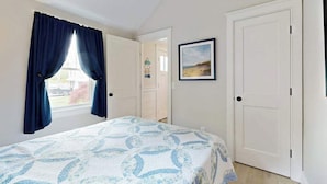A bedroom with a bed, a window with curtains, a door, and a framed picture on the wall. - Beautifully remodeled cottage near the beach with central AC, gas grill & lawn (Orleans)