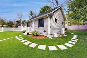 A single-story house with a front porch, a small garden, and a white picket fence. - Beautifully remodeled cottage near the beach with central AC, gas grill & lawn (Orleans)