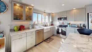 A modern kitchen with white cabinetry, a built-in oven, and a dining area with a marble table. - Cozy cottage steps to the beach with patio, W/D, & partial AC (North Truro)