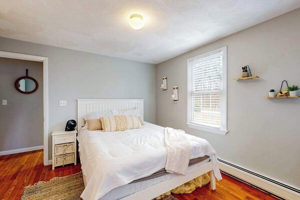 A bedroom with a bed, bedside tables, a mirror, a window with blinds, and wall-mounted shelves. - North Falmouth House: Near Beach, Fire Pit, & Dog-Friendly! (North Falmouth)