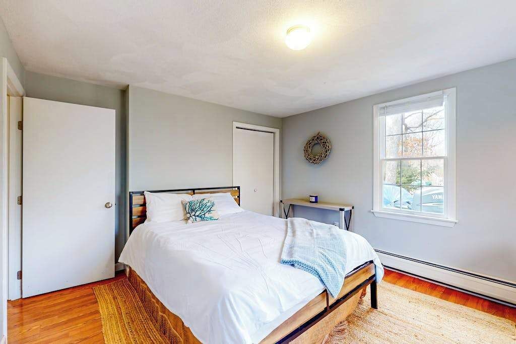 Un dormitorio con cama, puerta, ventana y lámpara fijada a la pared.