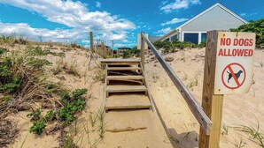 Ein Strand mit einer Holztreppe, die zu einem Gebäude führt, und einem Schild mit der Aufschrift 'KEINE HUNDE ERLAUBT'.