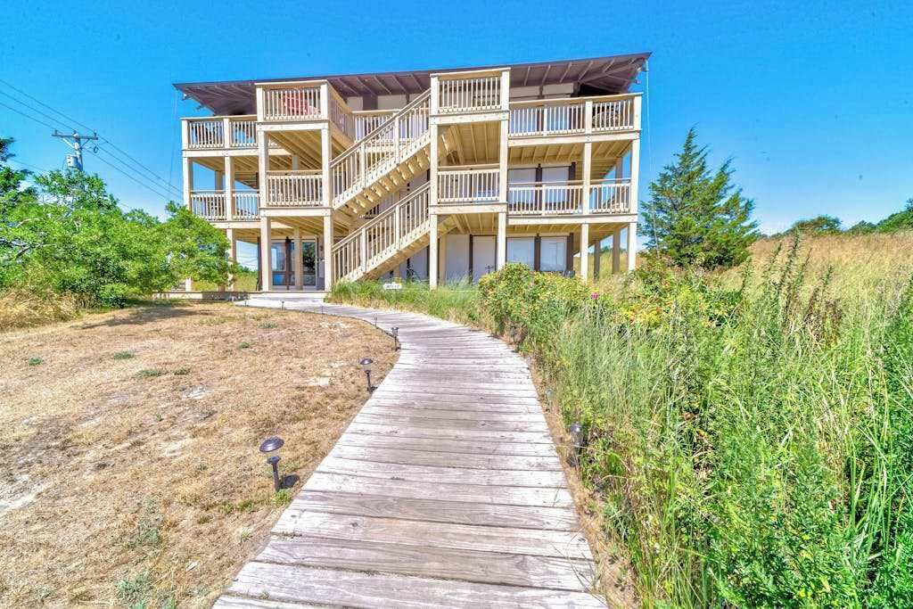 A multi-story building with balconies and a wooden pathway leading to it.