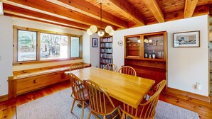 A wooden dining table with chairs, a bookshelf, and a window with a view of trees. - Private location, Gas Grill, A/C, Wi-Fi, Washer/Dryer (Wellfleet)