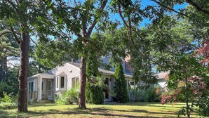 A single-story house with a front porch, surrounded by trees and a well-maintained lawn. - Private location, Gas Grill, A/C, Wi-Fi, Washer/Dryer (Wellfleet)