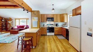 A kitchen with wooden cabinets, a white refrigerator, and a dining area with a table and chairs. - Private location, Gas Grill, A/C, Wi-Fi, Washer/Dryer (Wellfleet)