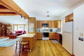 Una cocina con armarios de madera, un refrigerador blanco y una zona de comedor con mesa y sillas.
