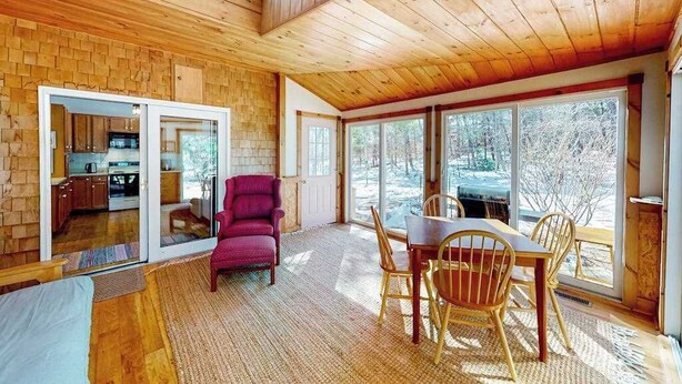 A wooden interior with a dining area, a red chair, and a view through large windows. - Private location, Gas Grill, A/C, Wi-Fi, Washer/Dryer (Wellfleet)