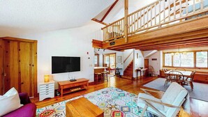 A spacious living area with a wooden staircase, a television, a sofa, and a dining table. - Private location, Gas Grill, A/C, Wi-Fi, Washer/Dryer (Wellfleet)
