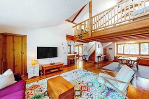 A spacious living area with a wooden staircase, a television, a sofa, and a dining table. - Private location, Gas Grill, A/C, Wi-Fi, Washer/Dryer (Wellfleet)
